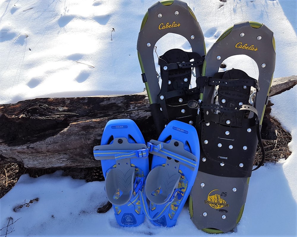 Two pairs of snowshoes next to a log along the Roof Trail.::Snowshoes in a variety of sizes are available at Jewel Cave.