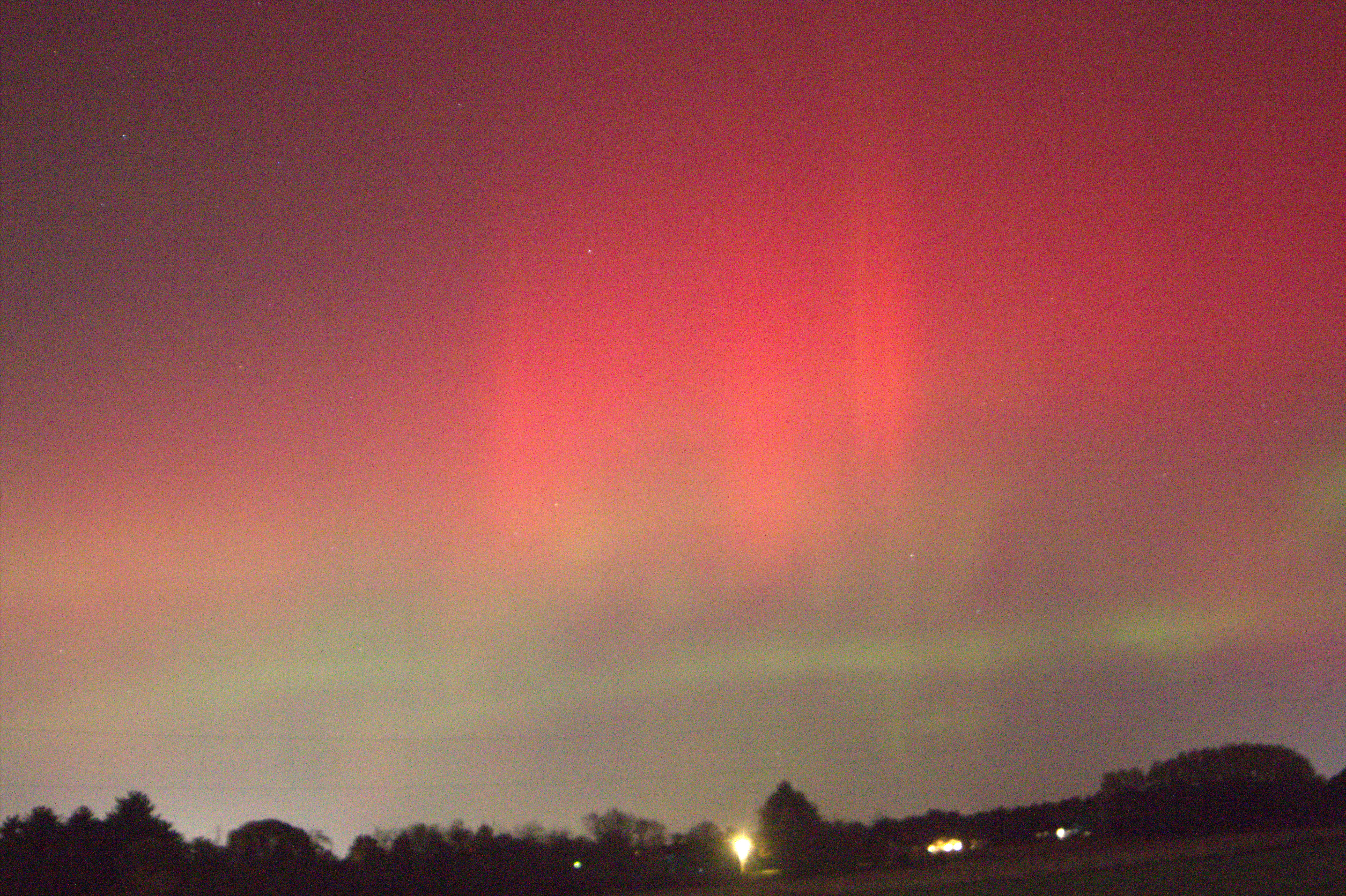 A night sky showing clouds of pink and green, with shadows of buildings at the horizon