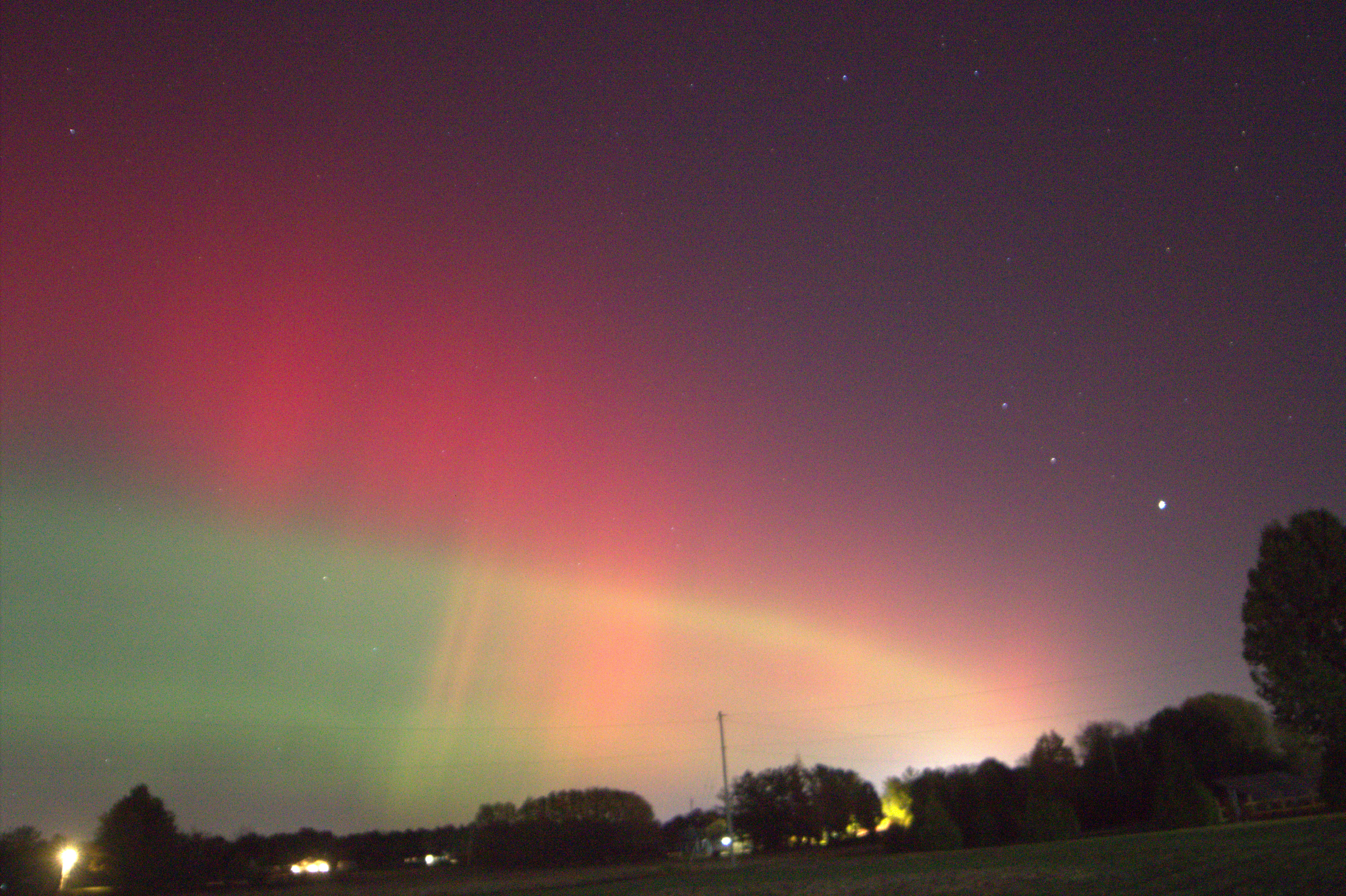 A night sky showing clouds of pink and green, with shadows of buildings at the horizon