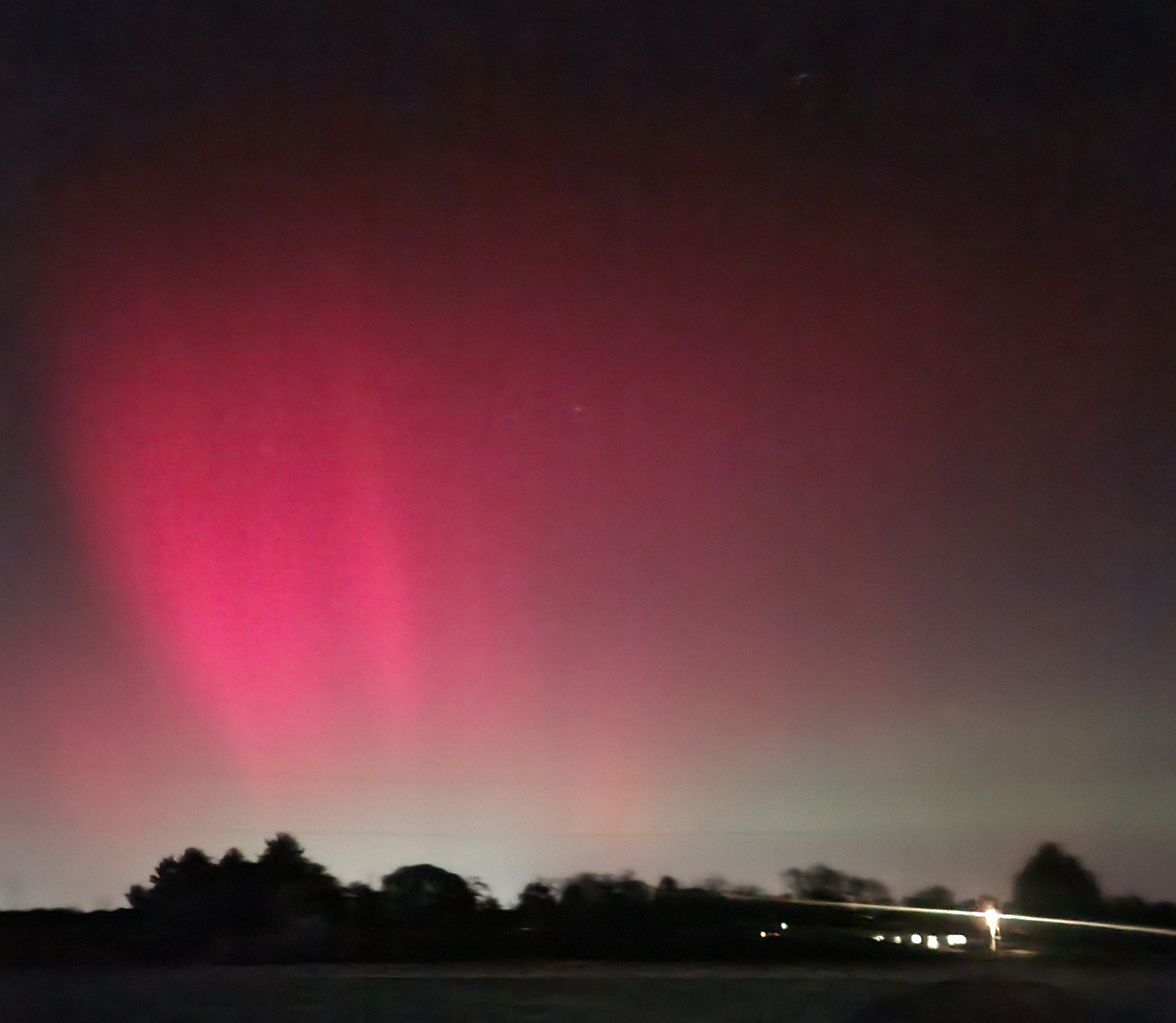 A night sky showing clouds of pink and green, with shadows of buildings at the horizon