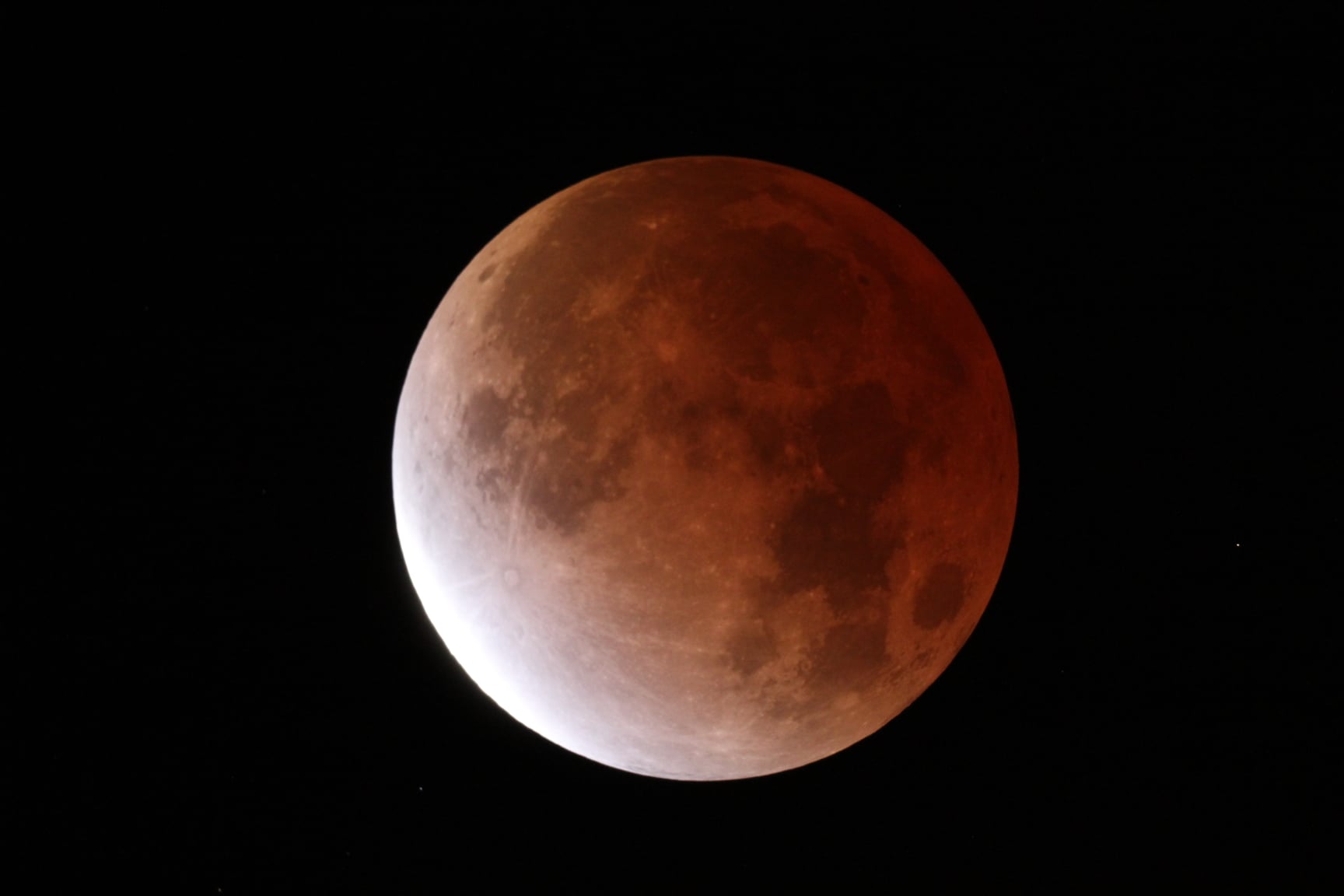 Orange and white disk surrounded by black sky.