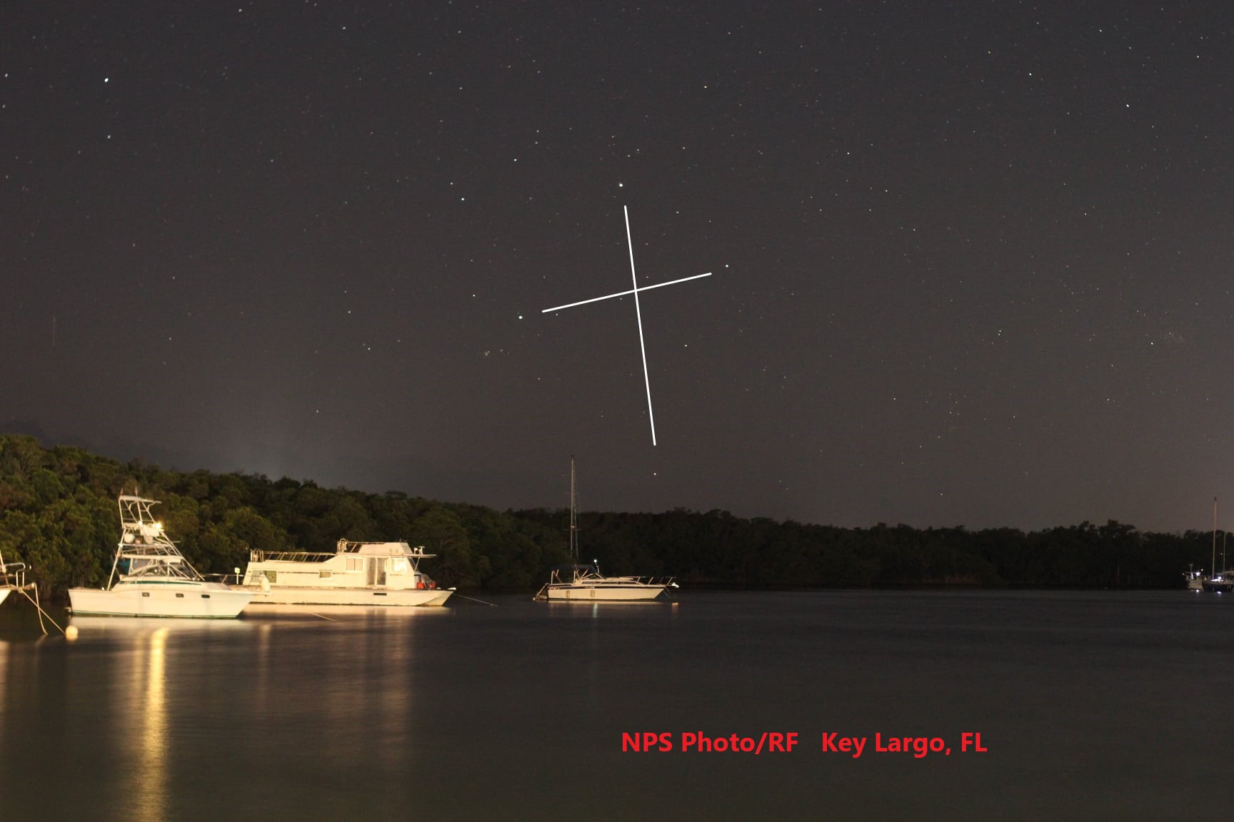 A picture containing a lake, boats in the water, trees, and stars in the form of a cross.