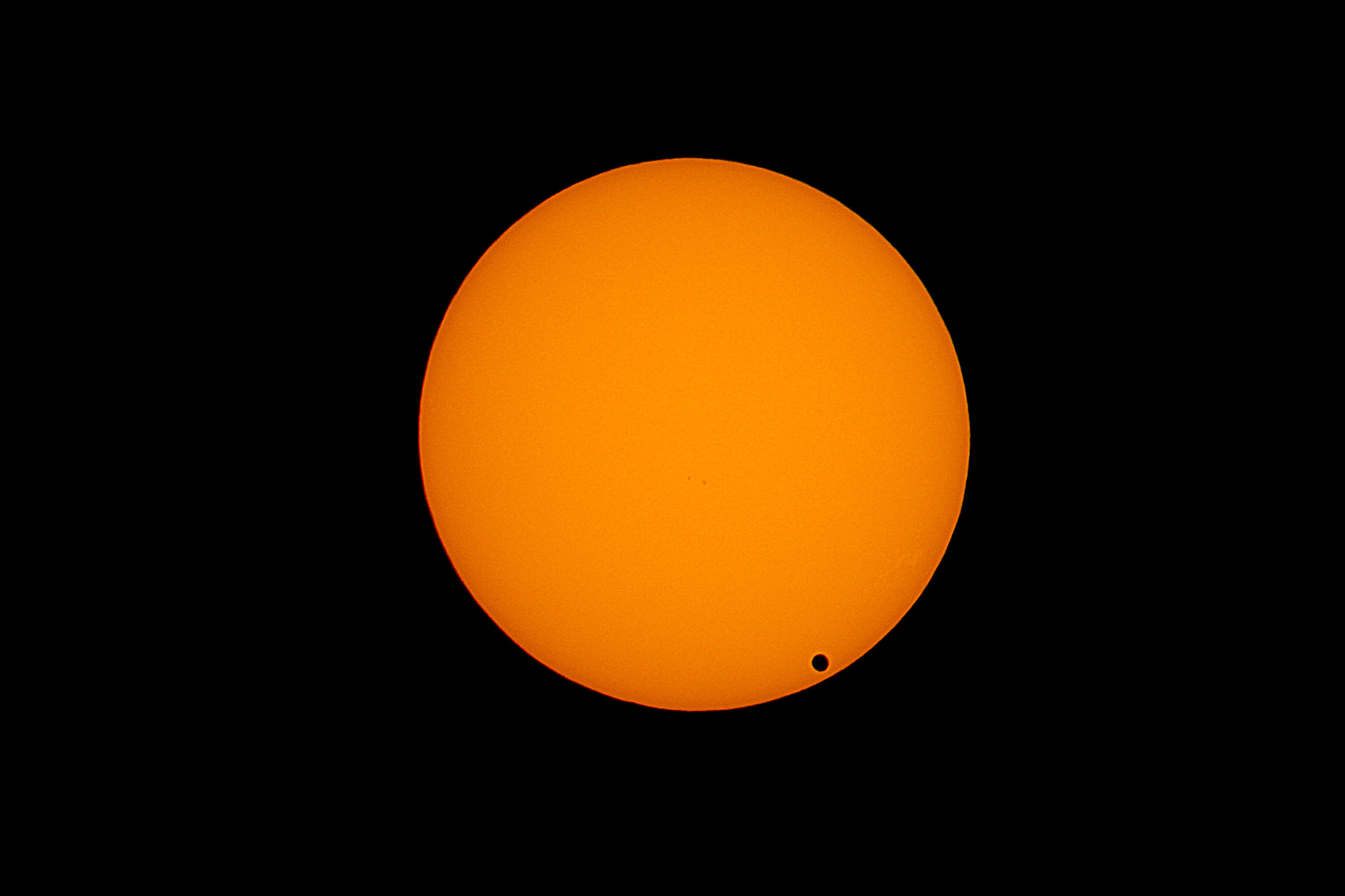 Orange ball with tiny black dot inside, surrounded by black space.