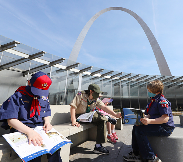 Three children in Boy Scout Uniforms sitting on chairs in front of the Gateway Arch.