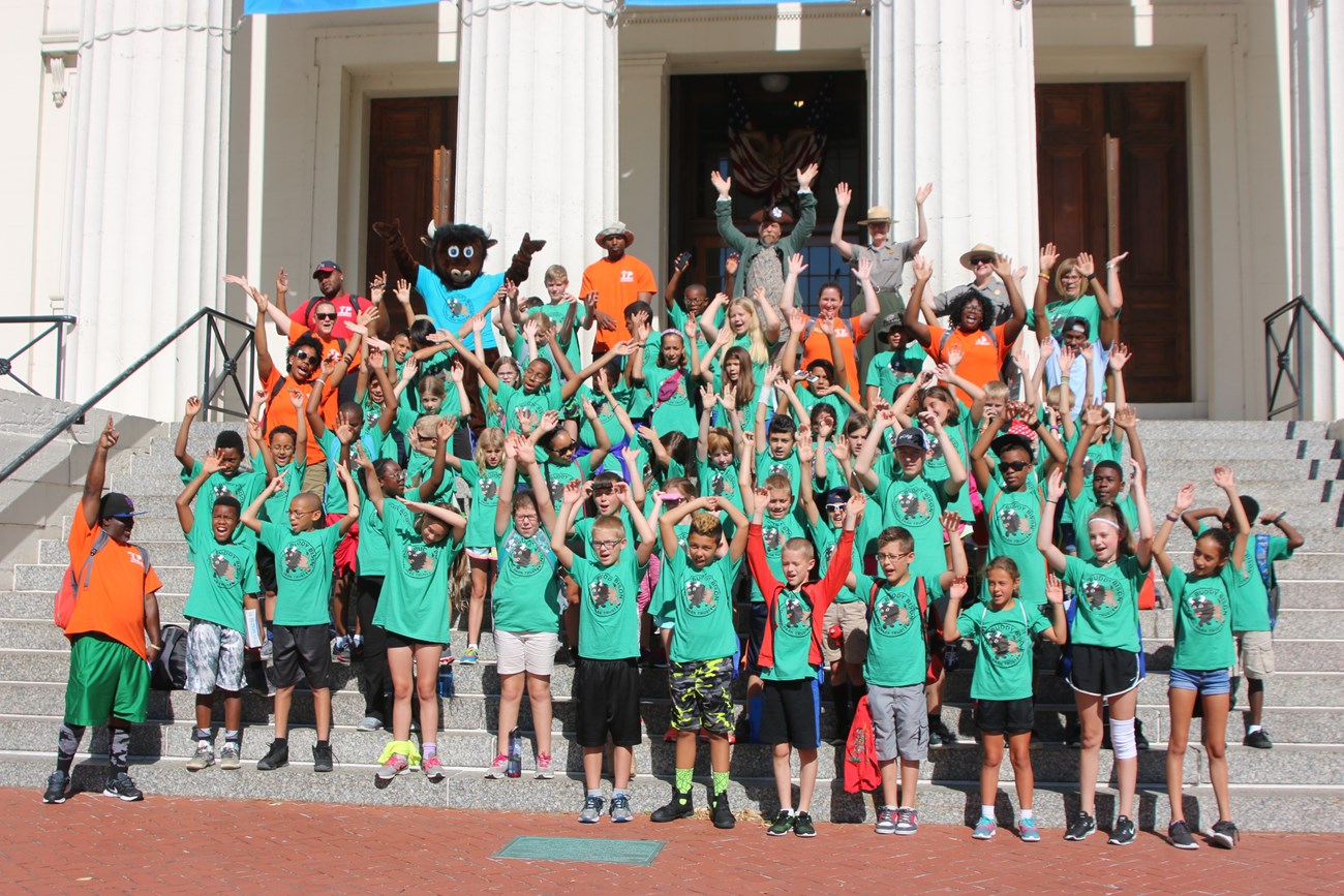 Large group of people on the steps of a courthouse with their hands raised and posing for a photo.