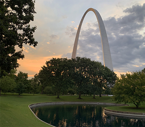Arch South Pond South pond in the foreground with the Gateway Arch in the background with an orange and blue sky. Green grass and trees surround the Arch and pond.