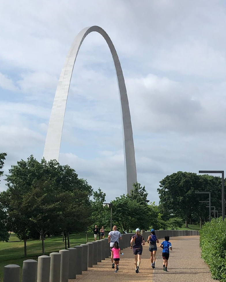 Group of of people running on the Arch grounds Group of people running on the Arch grounds. The gateway Arch is in the background.
