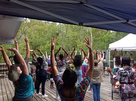 A dozen outdoor park visitors stretch by lifting their arms.