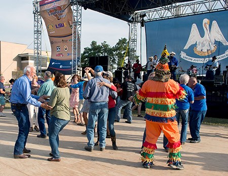 A band performing on a stage bearing a Louisiana state flag, with dancers in the foreground.