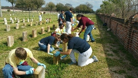 Volunteers with brushes and buckets cleaning military headstones in a cemetery
