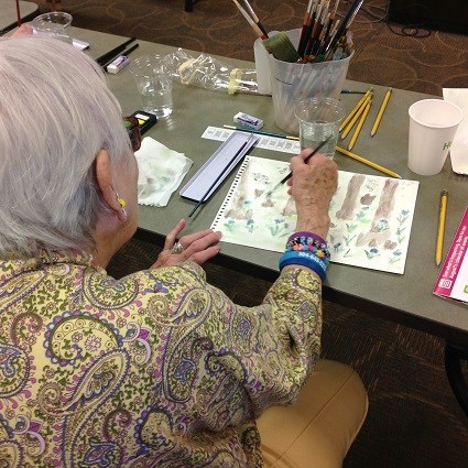 A woman holding a brush paints a scene of a cypress swamp with watercolor paints
