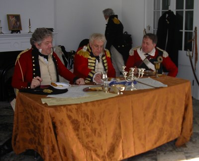Three British officers in red coats seated at a table, examining maps Three British officers in red coats seated at a table, examining maps