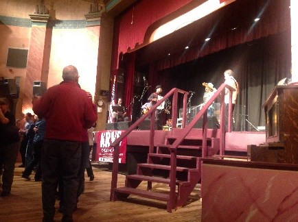 A Cajun band, led by an accordion player, performs onstage as the audience dances.