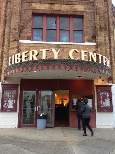 A man and a woman approach the ticket window of a theater building, under a lighted sign reading "Liberty Center"