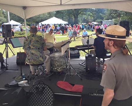 A park ranger stands backstage as a band plays beneath a tent.
