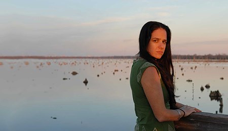 Monique Verdin stands outside, near open water in a coastal wetland.