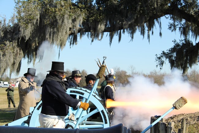 Men dressed as soldiers fire a cannon under a veil of Spanish moss.