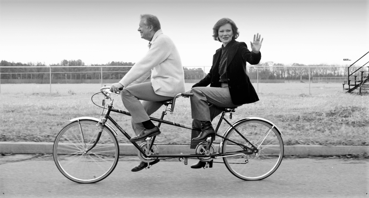 Jimmy and Rosalynn Carter ride a 2 seated bike down a street