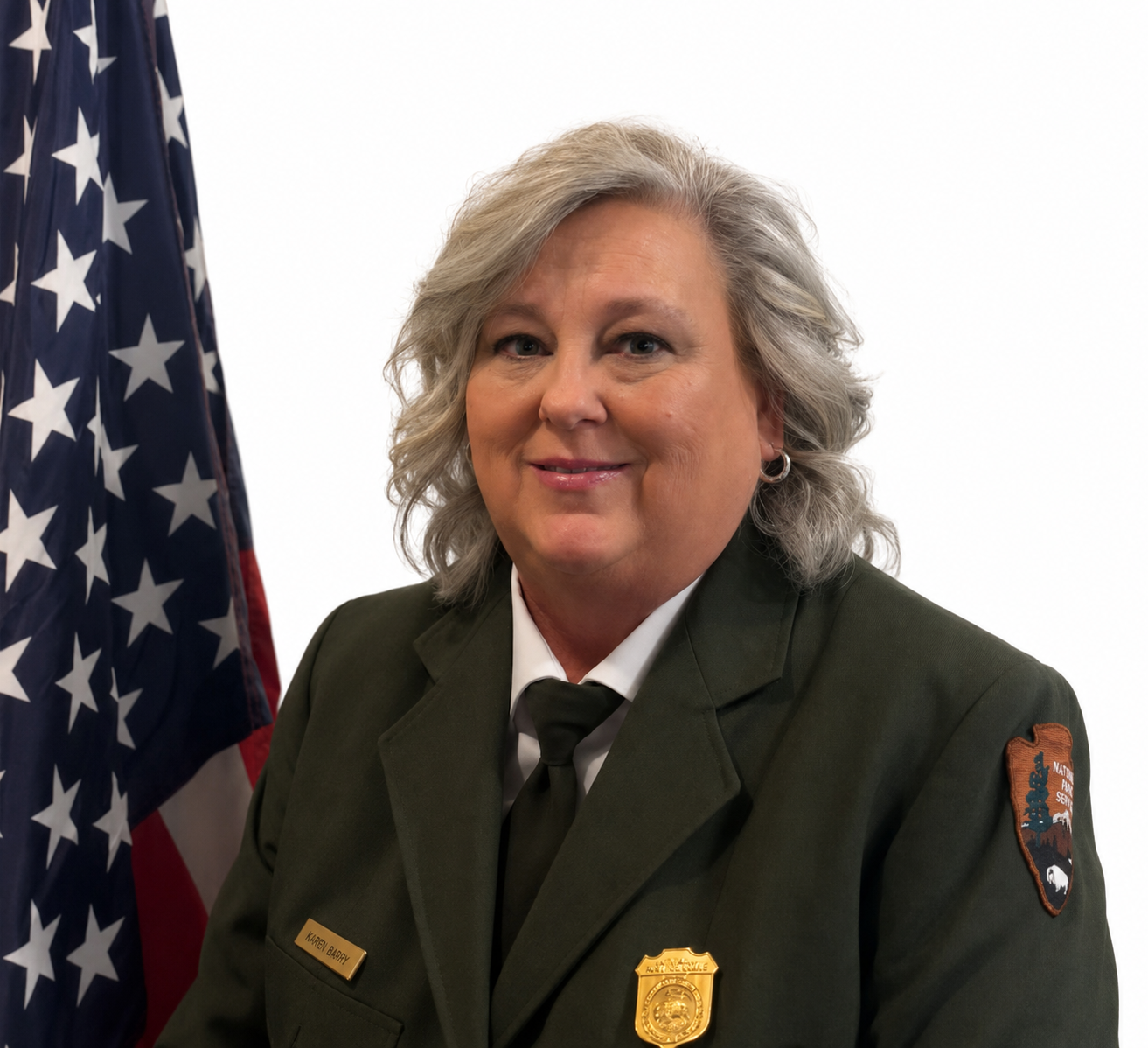 Official portrait of Superintendent Karen Barry smiling in a National Park Service uniform, with an American flag to her right.