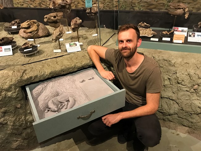 Artist Reid Psaltis sits near his artwork of a sculpted dog in an exhibit drawer.