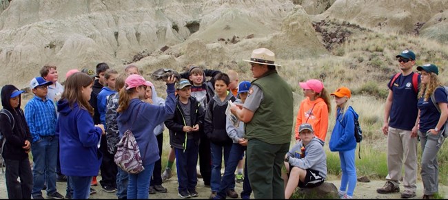 students surround a ranger during a field trip through badlands, landscape without plants
