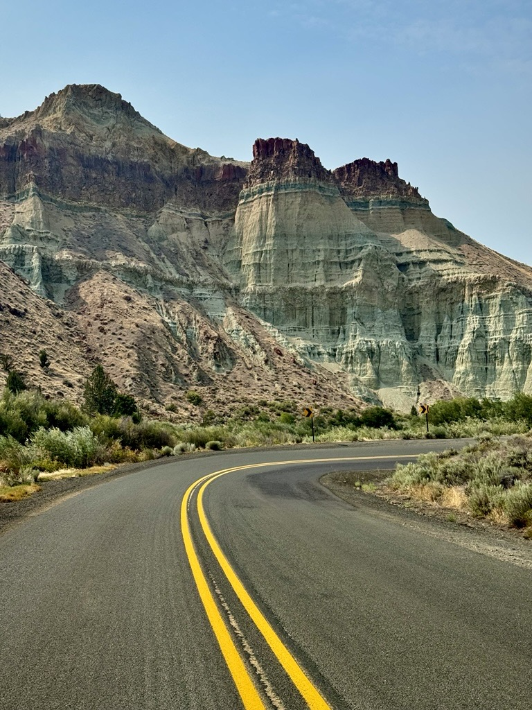 Cathedral Rock rises prominently, displaying dramatic layers of pale green, tan, and reddish-brown sedimentary rock. The sky above is mostly clear with some smoky haze, adding contrast to the striking colors and textures of the landscape