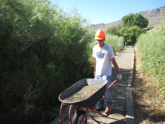 Youth Conservation Corps Member a young person holds a wheel barrel while walking along a trail