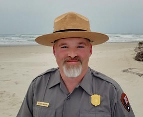Patrick Gamman Superintendent Patrick Gamman image from bust up in his Park Service uniform and flat-hat taken in front of a sandy beach.