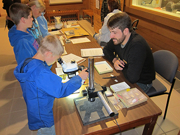 The former park's paleontologist shows three children how to use microscopes while studying fossils.