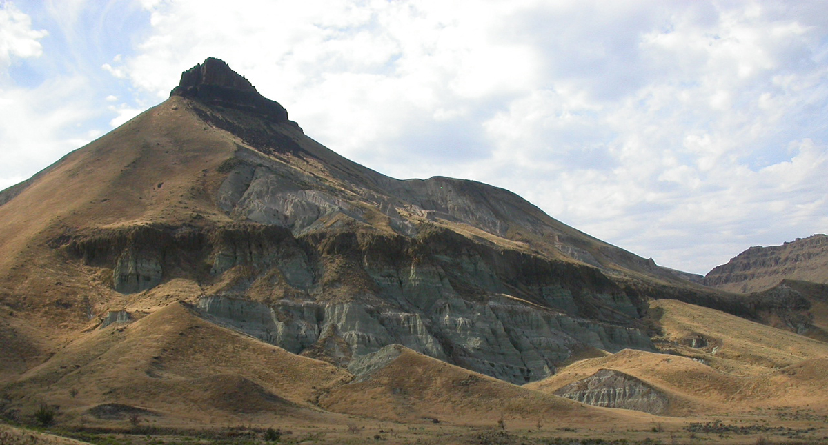 A slanted rocky hillside with green and blue layers on a partly cloudy day