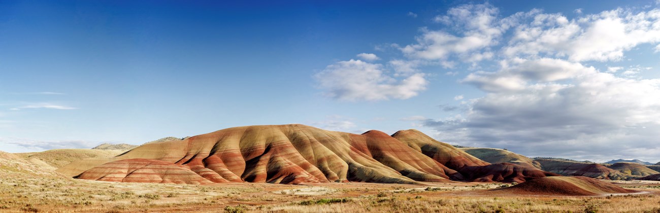 Red and yellow striped hills with cloudy blue skies above.