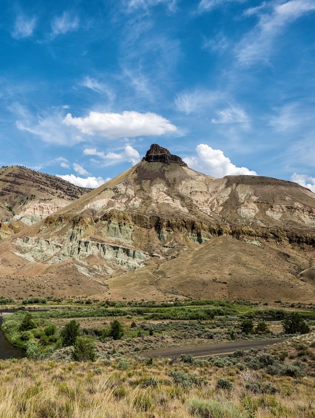 Sheep Rock is an outcropping - not quite a hill but not quite a mountain. It is vaguely pyramid shaped, with a basalt capstone and blue-green and pink sedimentary layers below.