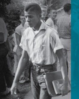 An African-American student with books under his arm walks through a crowd of white students