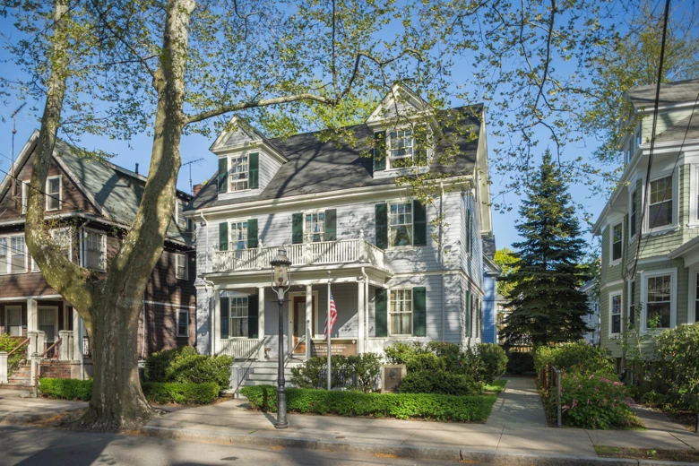 Kennedy family home at 83 Beals Street, Brookline A three story grey house with dormers in its roof.  An American flag is flying on a pole in front, and a gas lamp is on the sidewalk. A large street tree with light green leaves is on the sidewalk.