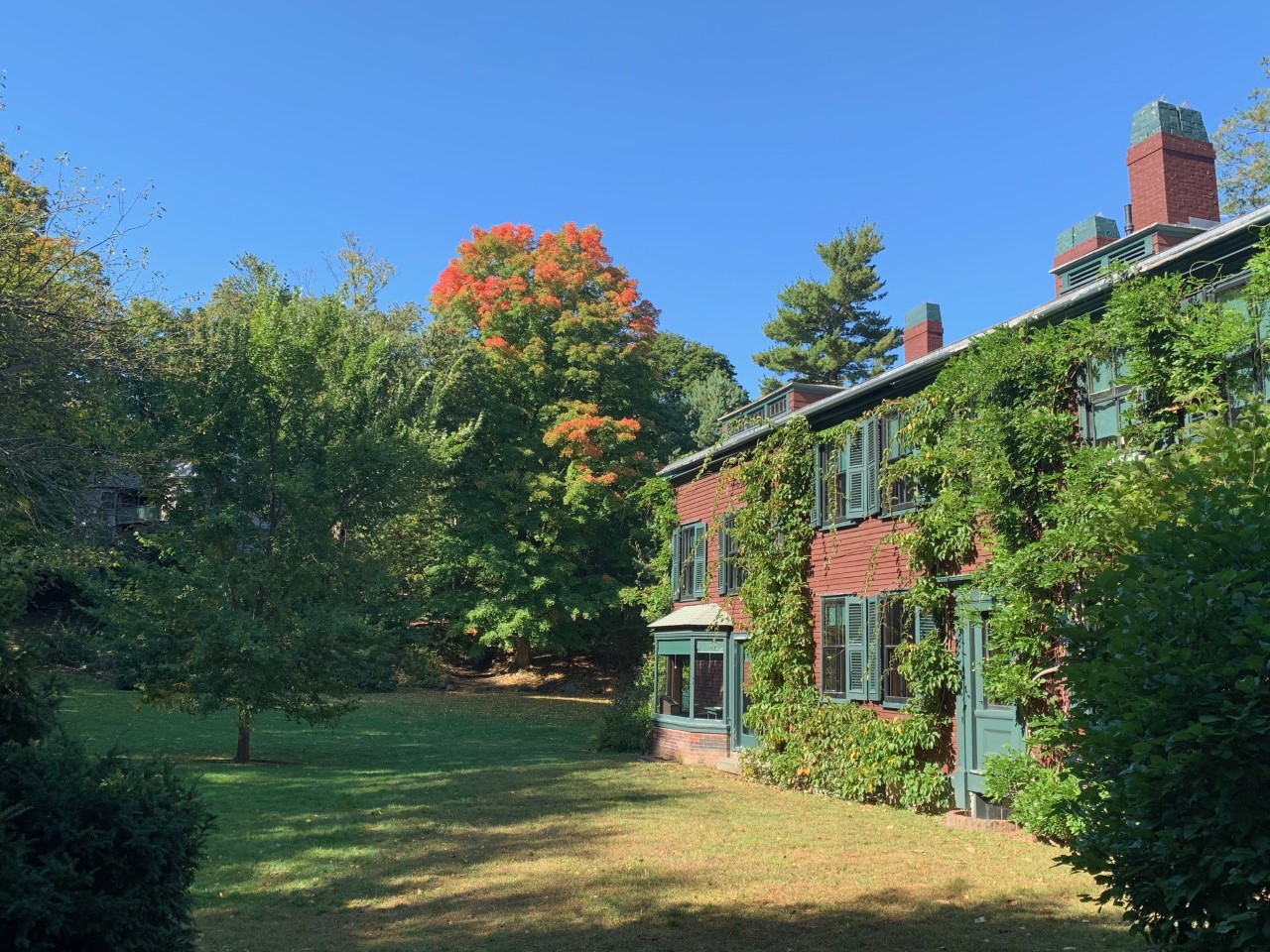 Red Building covered with ivy with a large lawn. Trees in background are beginning to change color.