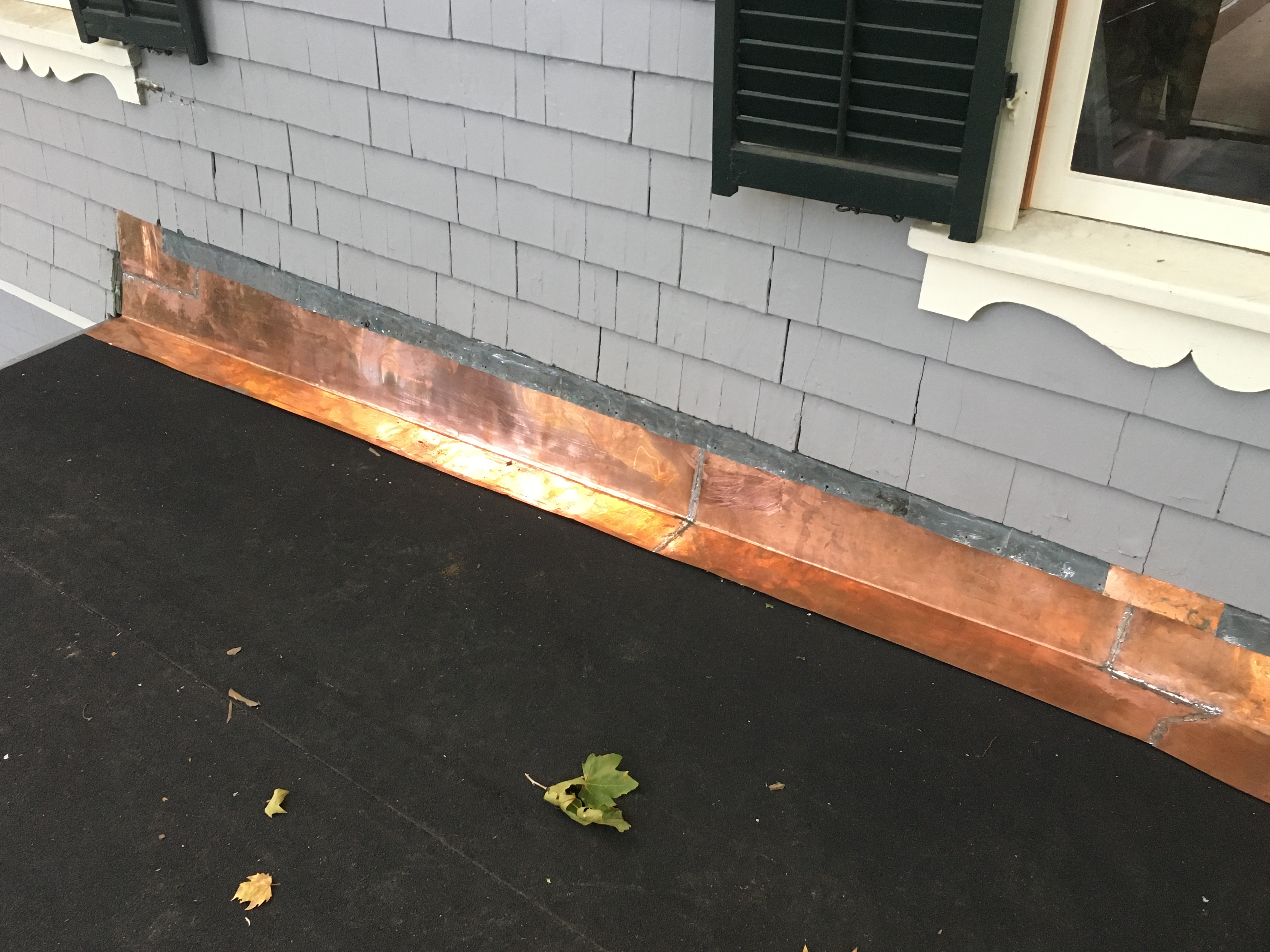 A copper strip separates gray plank siding and a black rooftop