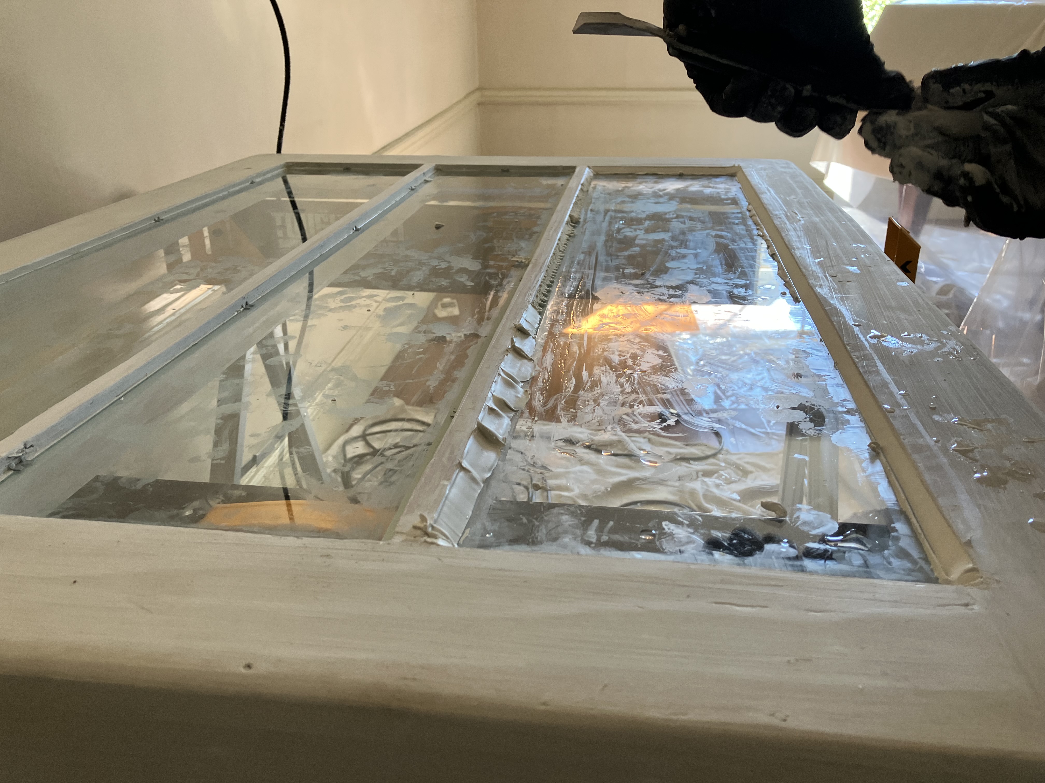 A white framed window is restored by a maintenance workers whose gloved hands show in the photo