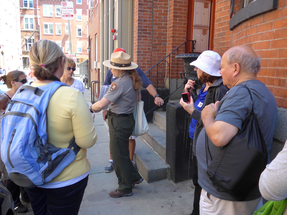 A ranger stands in downtown Boston, reading aloud a quotation. Behind her is Rose Kennedy's birthplace, a brick apartment building, in the North End. A ranger stands in downtown Boston, reading aloud a quotation. Behind her is Rose Kennedy's birthplace, a brick apartment building, in the North End.