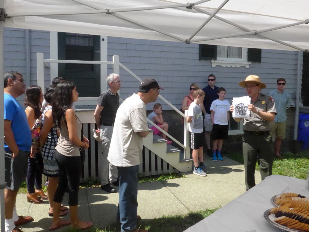 Visitors stand; a man leans in to see a photo during a backyard talk given by a ranger.