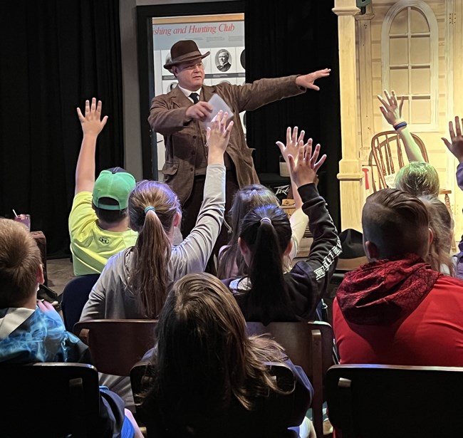 A park ranger in costume talks to a group of school students.