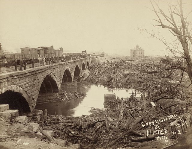 A stone railroad bridge with seven arches with flood debris in front of it.