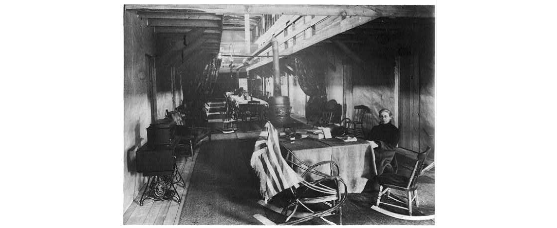 The interior of a Red Cross hotel with a woman seated at a table.