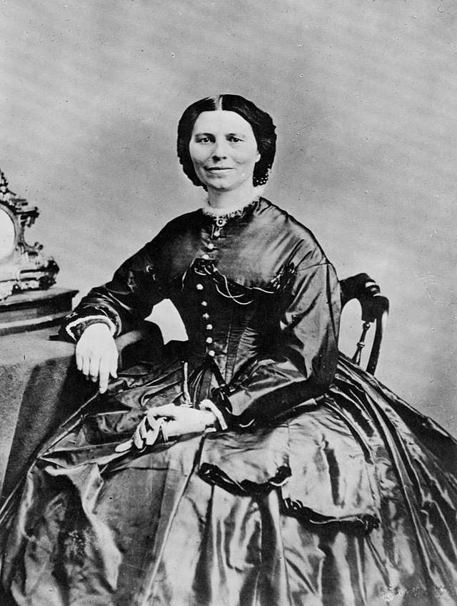 An image of a 19th century woman sitting in a chair holding gloves.