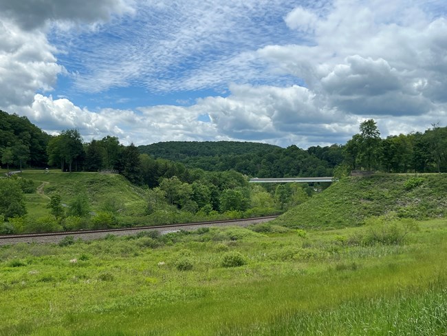Grass covered earthen dam with an empty space in the middle.
