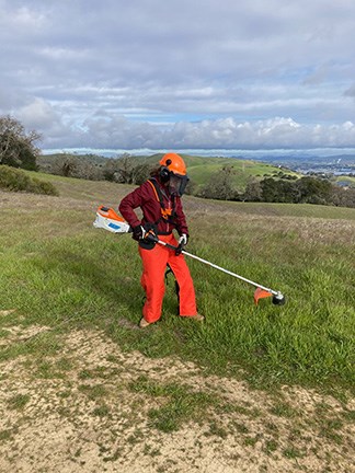 Young woman in full gear using a weed whacker on Mt. Wanda
