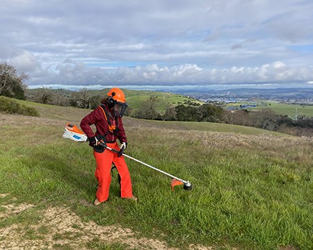 Young woman in full gear using a weed whacker on Mt. Wanda