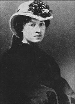 Louie Muir. Young woman in a hat and dress, sitting.