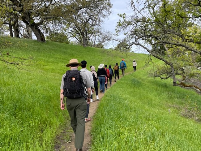 Male ranger and various visitors hike along a nature trail.