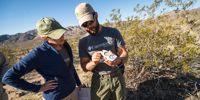 two volunteers wearing Earthwatch shirts look at a clinometer two volunteers wearing Earthwatch shirts look at a clinometer