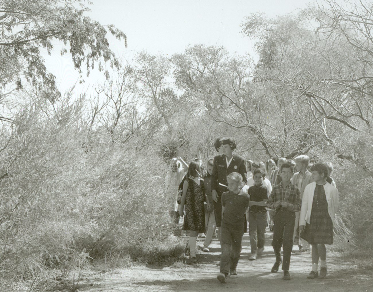 photo from the 1960s showing a group of children walking in the desert with a woman ranger